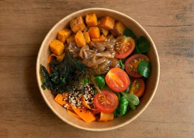 Eine farbenfrohe „Ma' Anu“ Bowl von Bowls4 in Gera, angerichtet in einer nachhaltigen Bowl-Schale. Man sieht eine reichhaltige Füllung aus gebackenen Süßkartoffeln, Karotten, proteinreichem Quinoa, frischem Feldsalat und knusprigen Grünkohl-Chips, garniert mit fruchtigem Zwiebelchutney.