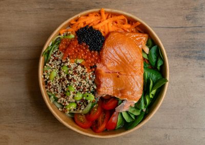 Draufsicht der Ma Kai Bowl von Bowls4 in Gera: Eine gesunde Bowl mit einem großen Lachsfilet, Quinoa, Edamame, Karottenstreifen, Tomaten und Lachs-Kaviar, serviert in einer Holzschale. Auch glutenfrei erhältlich.
