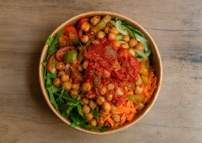Draufsicht der veganen Ma Kanu Bowl von Bowls4 in Gera: Eine nachhaltige Pappschale gefüllt mit Kichererbsen, einer würzigen Tomatensalsa, Karottenstreifen, Gurken, Rucola und Tomaten. Auch glutenfrei erhältlich.