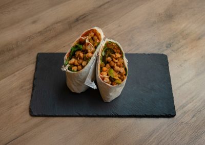 Draufsicht des halbierten „Ma Owilli Kanu“ Wraps von Bowls4 in Gera: Der vegane Wrap liegt auf einer Schieferplatte und zeigt die Füllung aus Kichererbsensalat, Tomatensalsa und Rucola. Auch glutenfrei erhältlich.