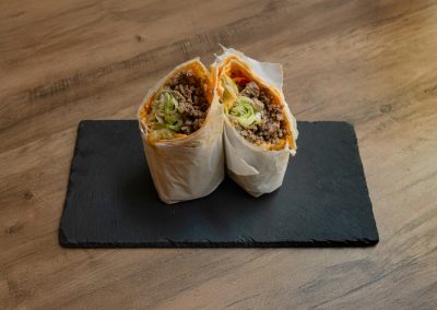 Der „Ma Owilli Kino“ Cheeseburger-Wrap von Bowls4 in Gera, halbiert auf einer Schieferplatte. Der Wrap ist prall gefüllt mit saftigem Hackfleisch (Schwein/Rind), Eisbergsalat und geschmolzenem Käse. Auch glutenfrei erhältlich.